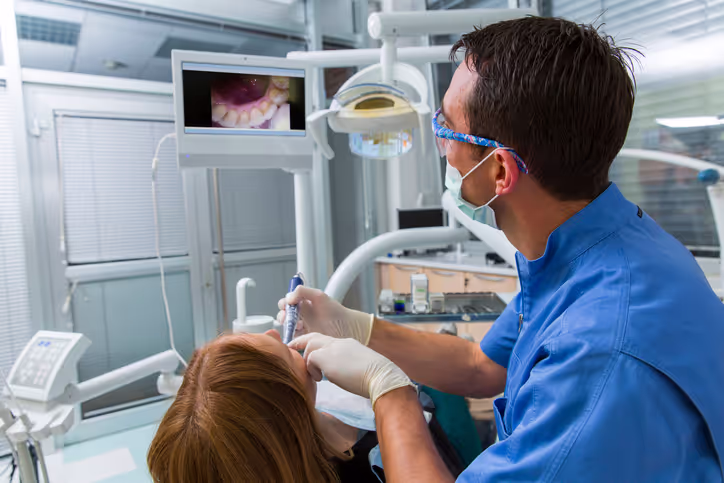 Dentist using an intraoral camera on a patient while viewing teeth images on a monitor in a dental clinic.