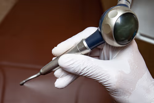 Close-up of a gloved hand holding a dental prophy jet polisher tool.