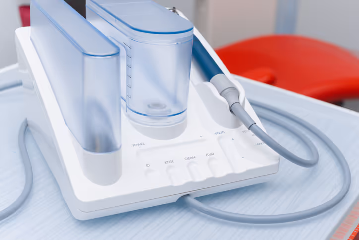 Close-up of a white ultrasonic dental scaler unit with water containers and a handpiece on a dental tray.