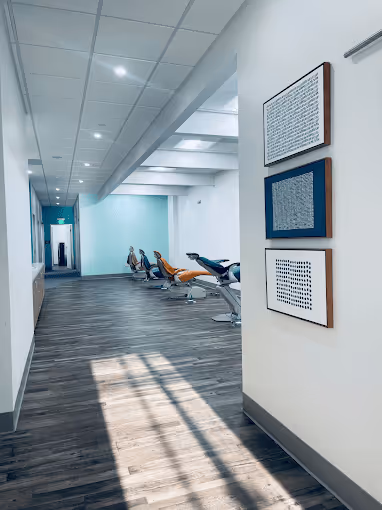 Hallway with wood flooring leading to a row of reclining chairs in a brightly lit modern interior.
